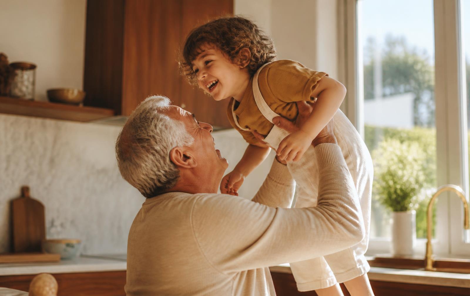 A grandfather lifting his laughing grandchild in a warm kitchen